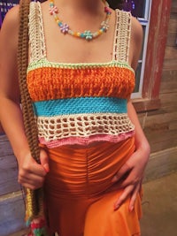 a woman wearing an orange crochet top and necklace