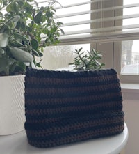 a black and brown crocheted bag sitting on a table next to a potted plant