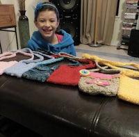 a young girl smiles in front of a table full of crocheted purses