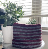 a crocheted beanie on a table next to a potted plant